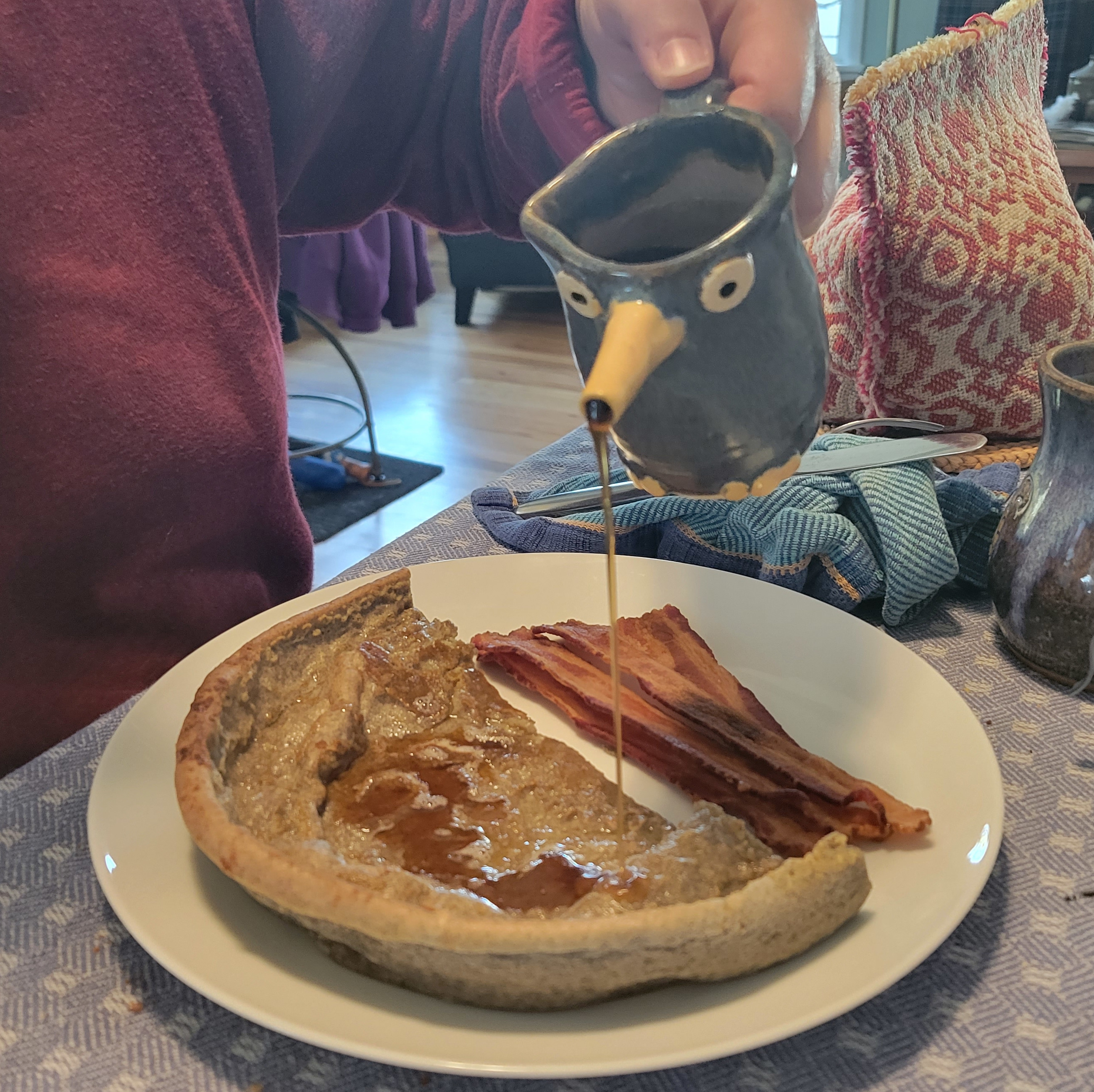 pouring a stream of syrup from a syrup bird onto a dutch baby pancake