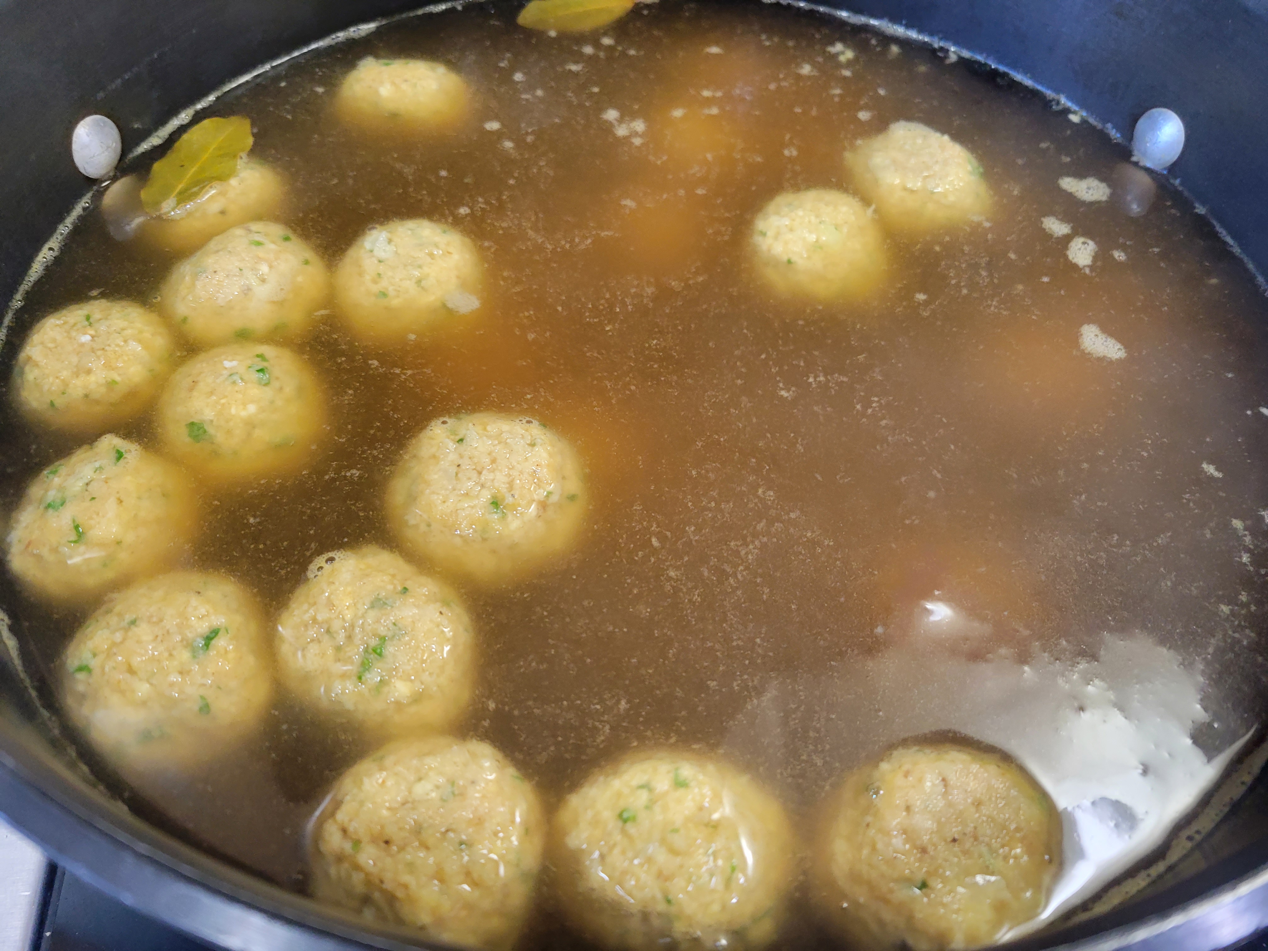matzoh balls starting to cook in a pot of boiling stock