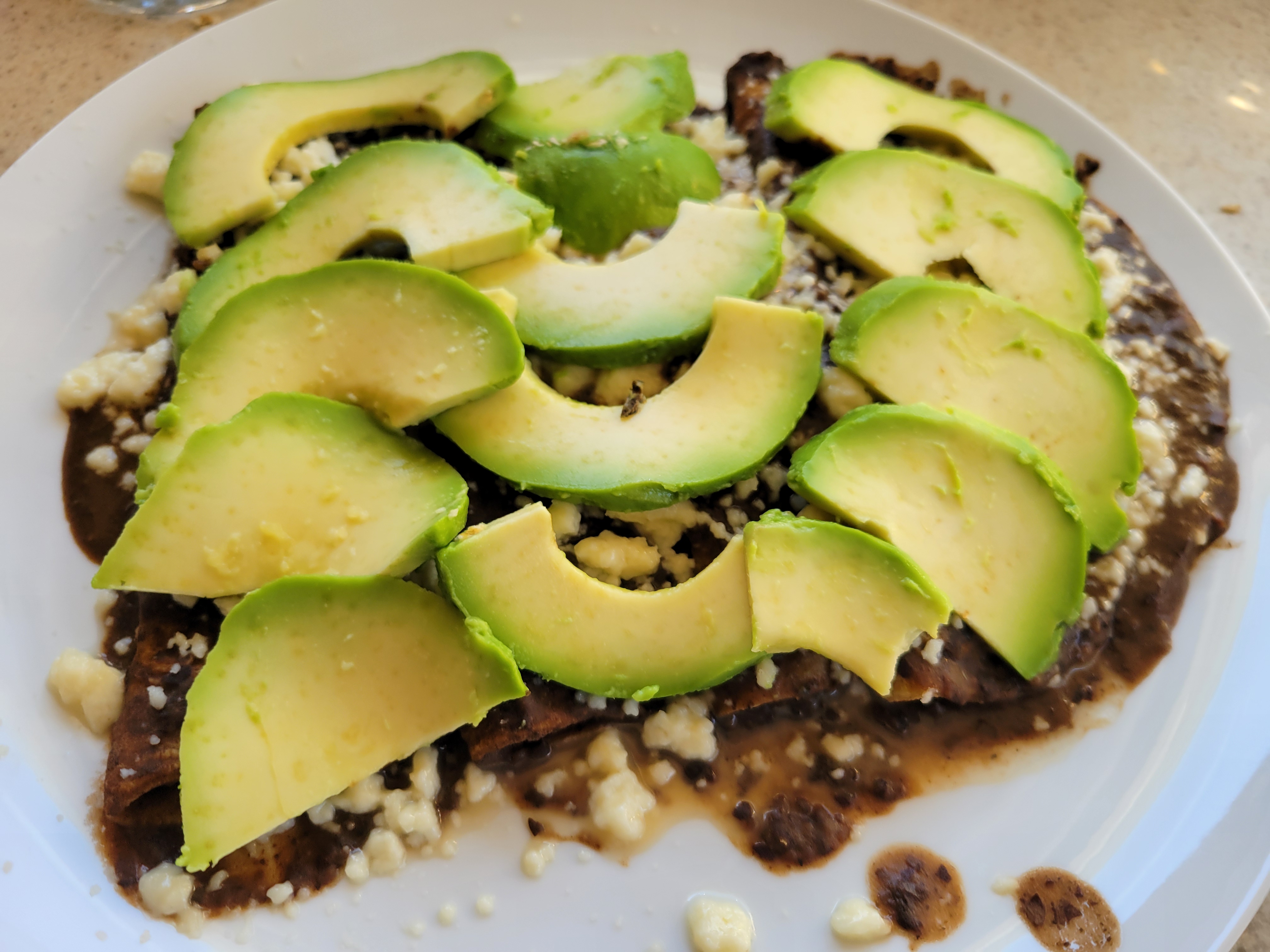 photo of a plate of enfrijoladas, tiled with slices of avocado