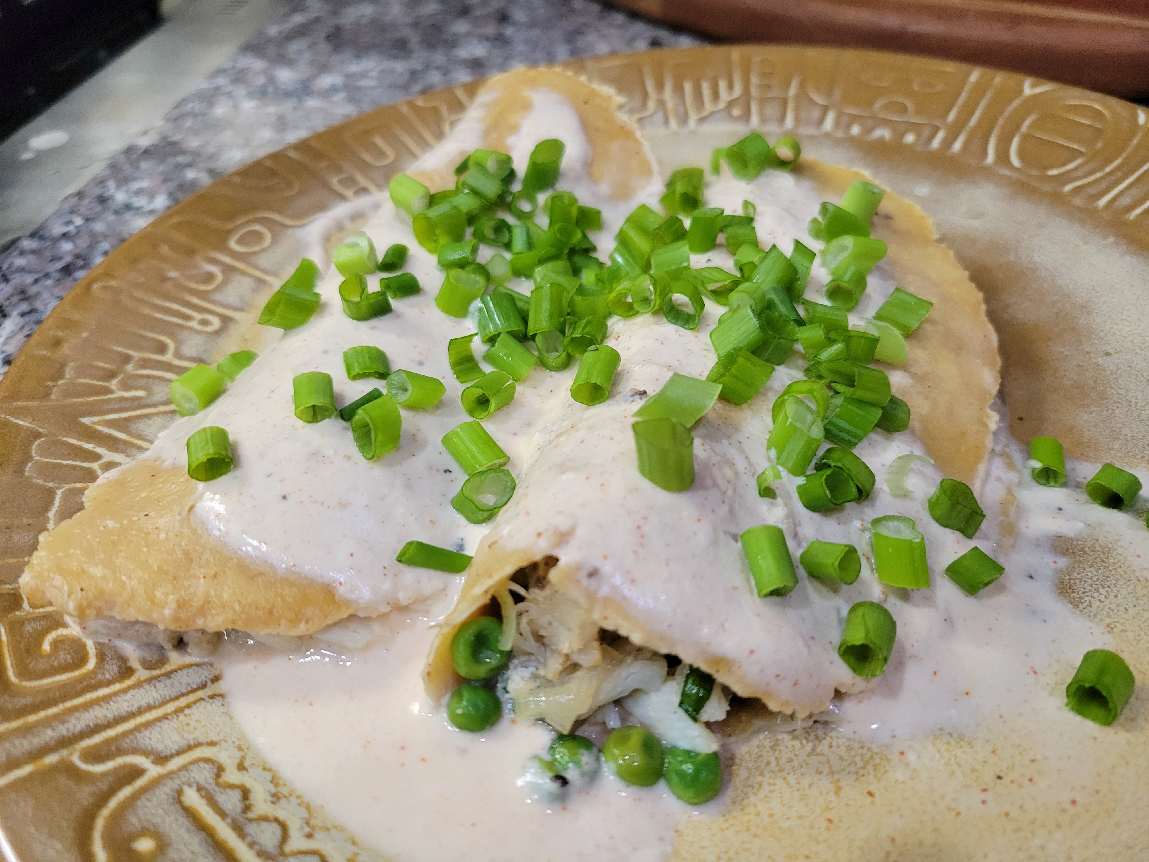 two folded-over enchiladas, coated in a thick cream sauce, filled with crab and peas