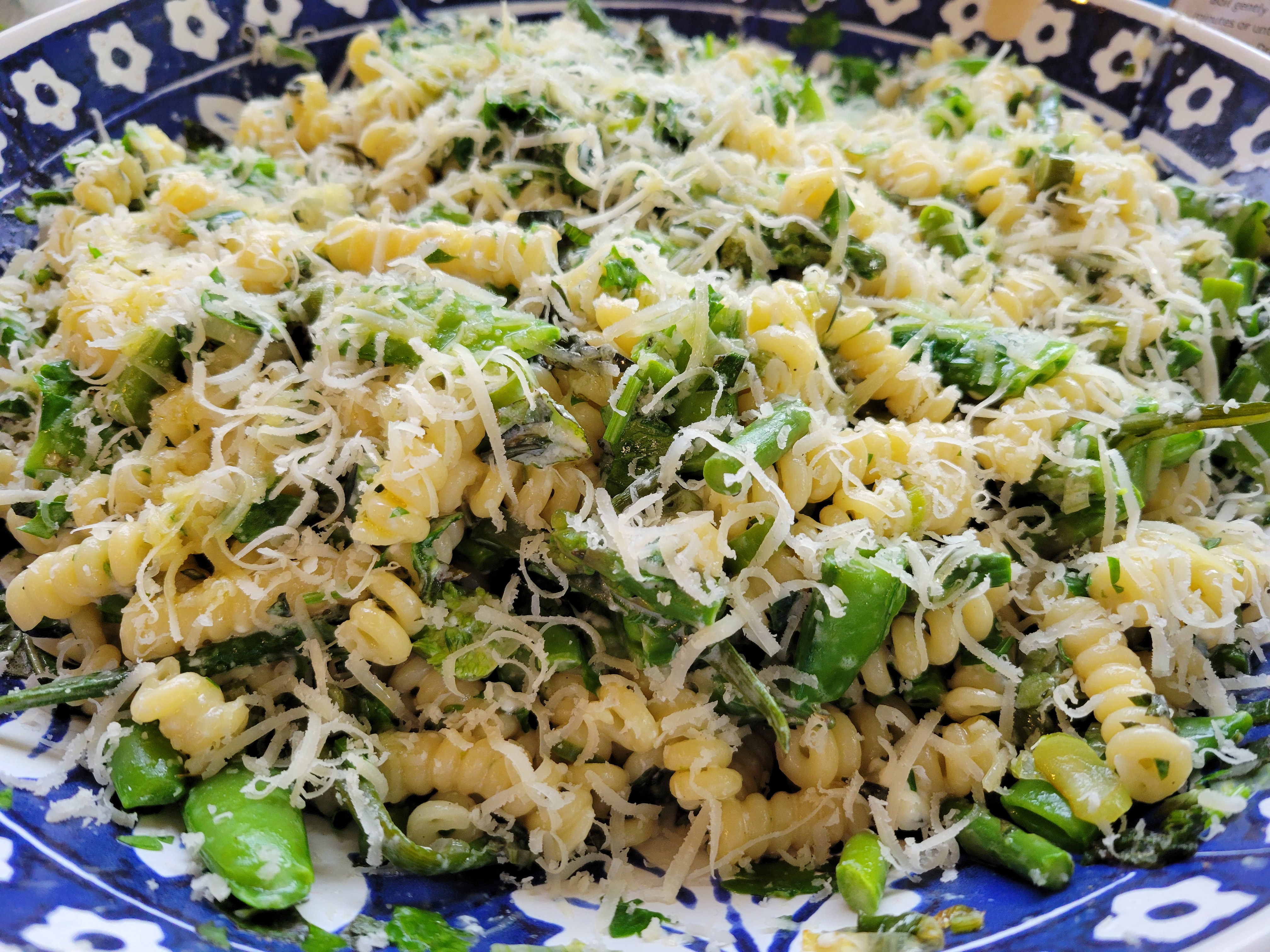 photo of a large serving bowl full of curly pasta with green vegetables and cheese