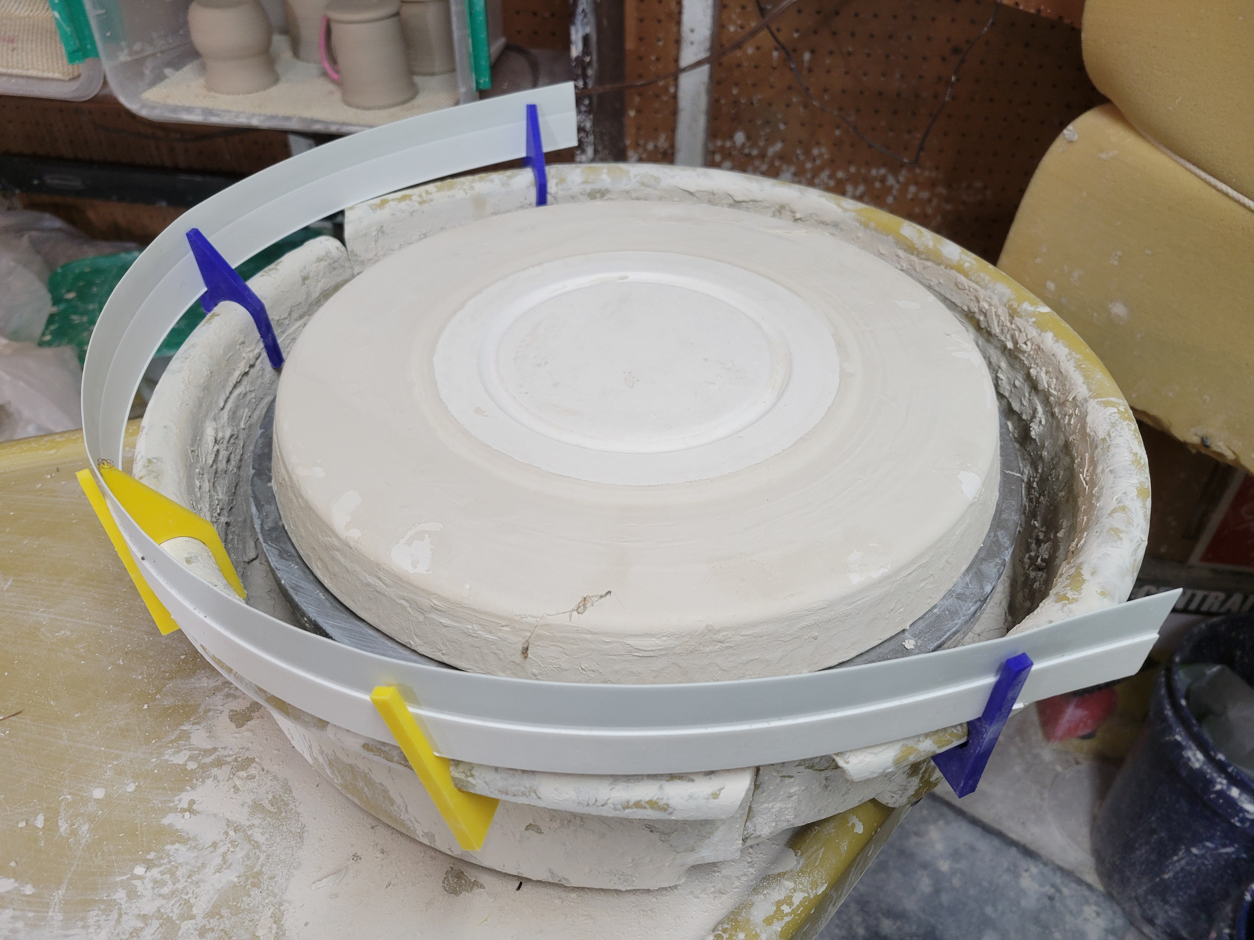 photo of a Brent pottery wheel, with clips on the splash pan, holding a strip of plastic as a sheild